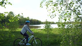 Den unga kvinnan som rider en cykel till och med, parkerar p? bakgrunden av en sj? eller en flod lager videofilmer Den unga kvinnan som rider en cykel till och med, parkerar p? bakgrunden av en sj? eller en flod lager videofilmer