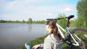 Den unga kvinnan som rider en cykel till och med, parkerar p? bakgrunden av en sj? eller en flod lager videofilmer Den unga kvinnan som rider en cykel till och med, parkerar p? bakgrunden av en sj? eller en flod lager videofilmer