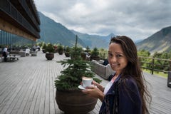 Den unga lyckliga kvinnan står på terrassen av hotellet med koppen kaffe royaltyfria foton Den unga lyckliga kvinnan står på terrassen av hotellet med koppen kaffe royaltyfria foton