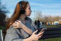 Den unga lyckliga rödhåriga mannen som flickan i parkerar på våren nära floden, lyssnar till musik till och med trådlös bluetooth royaltyfri fotografi Den unga lyckliga rödhåriga mannen som flickan i parkerar på våren nära floden, lyssnar till musik till och med trådlös bluetooth royaltyfri fotografi