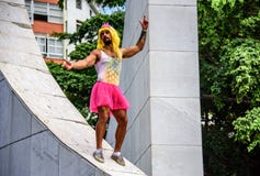 Den unga mannen i rosa färger krönar, den gula peruken, bodyen med ananas och det ljusa rosa ballerinakjolkjolanseendet på den mi royaltyfria foton Den unga mannen i rosa färger krönar, den gula peruken, bodyen med ananas och det ljusa rosa ballerinakjolkjolanseendet på den mi royaltyfria foton