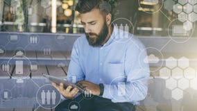 Den unga skäggiga hipstermannen sitter och använder den digitala minnestavlan I förgrund är faktiska symboler med folk, digitala fotografering för bildbyråer Den unga skäggiga hipstermannen sitter och använder den digitala minnestavlan I förgrund är faktiska symboler med folk, digitala fotografering för bildbyråer