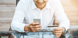 Den unga stiliga mannen tycker om att shoppa direktanslutet på mobiltelefonen med kreditkorten arkivbilder Den unga stiliga mannen tycker om att shoppa direktanslutet på mobiltelefonen med kreditkorten arkivbilder
