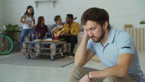Den unga studentgrabben känner rubbning och isolerade medan hans vänner som hemma firar partiet inomhus stock video Den unga studentgrabben känner rubbning och isolerade medan hans vänner som hemma firar partiet inomhus stock video