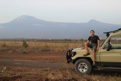 Den vita Caucasian handelsresanden i sportswear sitter i en jeep på bakgrunden av Mount Kilimanjaro royaltyfri fotografi Den vita Caucasian handelsresanden i sportswear sitter i en jeep på bakgrunden av Mount Kilimanjaro royaltyfri fotografi
