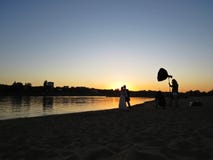 Den yrkesmässiga fotografen Photo Session med precis gift Nyligen-gifta sig par på stranden under solnedgång royaltyfri bild Den yrkesmässiga fotografen Photo Session med precis gift Nyligen-gifta sig par på stranden under solnedgång royaltyfri bild
