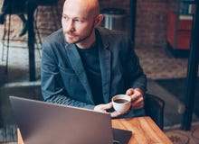 Denkende aantrekkelijke volwassen succesvolle kale gebaarde mens in kostuum met laptop in koffie stock foto Denkende aantrekkelijke volwassen succesvolle kale gebaarde mens in kostuum met laptop in koffie stock foto