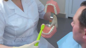 Dentist use jaw model and toothbrush to teach patient correct cleaning of teeth.
