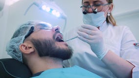Dentista en el trabajo en la oficina Un doctor de sexo femenino examina los dientes y los mandíbulas de un paciente masculino almacen de metraje de vídeo Dentista en el trabajo en la oficina Un doctor de sexo femenino examina los dientes y los mandíbulas de un paciente masculino almacen de metraje de vídeo