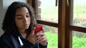 African American girl teenager depressed sitting by a window using her mobile cell phone or smartphone stock video African American girl teenager depressed sitting by a window using her mobile cell phone or smartphone stock video
