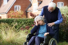Deprimierte ältere Frau im Rollstuhl, der vom Ehemann gedrückt wird Lizenzfreies Stockfoto