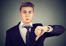 Der verärgerte enttäuschte junge Geschäftsmann, der Daumen unterzeichnen zeigt unten, in der Missbilligung Lizenzfreie Stockbilder Der verärgerte enttäuschte junge Geschäftsmann, der Daumen unterzeichnen zeigt unten, in der Missbilligung Lizenzfreie Stockbilder