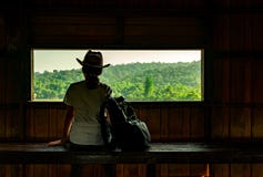 Desgaste de mujer asiático joven que el sombrero se sienta en banco de madera y hermosa vista de observación del bosque tropical fotografía de archivo Desgaste de mujer asiático joven que el sombrero se sienta en banco de madera y hermosa vista de observación del bosque tropical fotografía de archivo