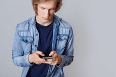 Det kantjusterade skottet av den manliga tonåringen i grov bomullstvillskjortan, modern smart telefon för håll, spelar lekar dire royaltyfri bild Det kantjusterade skottet av den manliga tonåringen i grov bomullstvillskjortan, modern smart telefon för håll, spelar lekar dire royaltyfri bild