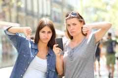 Deux amis fâchés tenant un téléphone avec des pouces vers le bas photographie stock Deux amis fâchés tenant un téléphone avec des pouces vers le bas photographie stock