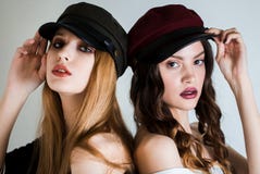Deux femmes dans des chapeaux et avec le maquillage lumineux sur le fond blanc de nouveau à arrière regardant l'appareil-photo Mo image libre de droits Deux femmes dans des chapeaux et avec le maquillage lumineux sur le fond blanc de nouveau à arrière regardant l'appareil-photo Mo image libre de droits