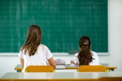 Deux filles s'asseyent aux bureaux d'école et regardent vers le tableau noir images stock Deux filles s'asseyent aux bureaux d'école et regardent vers le tableau noir images stock