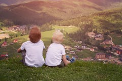 Deux garçons s'asseyant sur une colline et regardant les montagnes Dos vi Images libres de droits Deux garçons s'asseyant sur une colline et regardant les montagnes Dos vi Images libres de droits