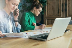 Deux jeunes femmes d'affaires s'asseyant dans le bureau à la table et au travail ensemble Sur des diagrammes d'ordinateur portabl image stock Deux jeunes femmes d'affaires s'asseyant dans le bureau à la table et au travail ensemble Sur des diagrammes d'ordinateur portabl image stock