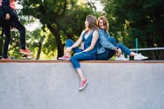 Deux jeunes filles heureuses s'asseyant au parc de patin image stock Deux jeunes filles heureuses s'asseyant au parc de patin image stock