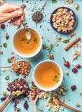 Deux tasses de tisane saine avec la menthe, cannelle, sèche se sont levées, la camomille fleurit dans les cuillères et la main du images stock Deux tasses de tisane saine avec la menthe, cannelle, sèche se sont levées, la camomille fleurit dans les cuillères et la main du images stock