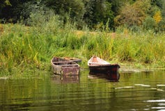 Deux vieux bateaux sur le rivage sont attachés à une vieille roue de voiture, sur un fond d'herbe verte images libres de droits Deux vieux bateaux sur le rivage sont attachés à une vieille roue de voiture, sur un fond d'herbe verte images libres de droits