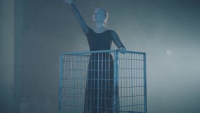 Diagramet av den yrkesmässiga ballerinadansen i svart klänning i studion i stor blå bur i den svarta bakgrunden med stock video Diagramet av den yrkesmässiga ballerinadansen i svart klänning i studion i stor blå bur i den svarta bakgrunden med stock video