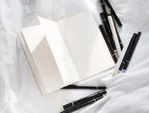 Diario aperto in bianco su un letto bianco con il mucchio delle penne immagine stock libera da diritti Diario aperto in bianco su un letto bianco con il mucchio delle penne immagine stock libera da diritti
