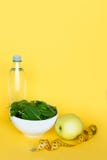 Dieta di concetto - alimento sano Linea dell'acqua, degli spinaci, della mela e del nastro su fondo giallo Copi lo spazio immagine stock Dieta di concetto - alimento sano Linea dell'acqua, degli spinaci, della mela e del nastro su fondo giallo Copi lo spazio immagine stock