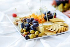 Different kinds of wine snacks: cheeses, crackers, fruits and olives on white table stock images Different kinds of wine snacks: cheeses, crackers, fruits and olives on white table stock images