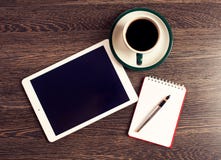 Digitale tabletcomputer met notadocument en kop van koffie op oud houten bureau