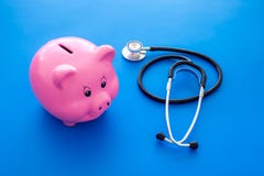 Dinero para el tratamiento Costos médicos Moneybox en la forma del cerdo cerca del estetoscopio en fondo azul foto de archivo Dinero para el tratamiento Costos médicos Moneybox en la forma del cerdo cerca del estetoscopio en fondo azul foto de archivo