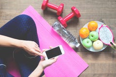 Direkt över av kvinnan i konditionkläder genom att använda mobiltelefonen med sportutrustningar och frukter på golvet, sunt Royaltyfri Foto Direkt över av kvinnan i konditionkläder genom att använda mobiltelefonen med sportutrustningar och frukter på golvet, sunt Royaltyfri Foto