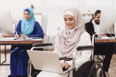 Disabled arab woman in wheelchair working in office. Woman is working on laptop. Stock Image Disabled arab woman in wheelchair working in office. Woman is working on laptop. Stock Image