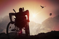 Disabled handicapped man has a hope. He is sitting on wheelchair and stretching hands at sunset