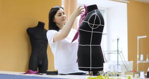 Diseñador de moda Works de la mujer joven en estudio El diseñador de la ropa está trabajando con los maniquíes de las medidas almacen de metraje de vídeo Diseñador de moda Works de la mujer joven en estudio El diseñador de la ropa está trabajando con los maniquíes de las medidas almacen de metraje de vídeo