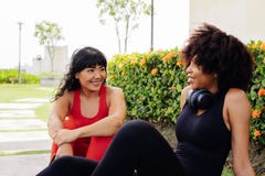 Diverse group of two female fitness friends taking break and talking in the park. Young women resting and smiling