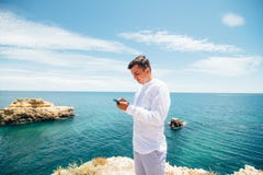 Divida le mie emozioni Il giovane felice sta scrivendo il messaggio a macchina sul telefono cellulare alla costa dell'oceano fotografie stock libere da diritti Divida le mie emozioni Il giovane felice sta scrivendo il messaggio a macchina sul telefono cellulare alla costa dell'oceano fotografie stock libere da diritti