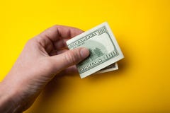 Doblado cientos billetes de dólar a disposición en un fondo, una venta o una compra amarilla foto de archivo Doblado cientos billetes de dólar a disposición en un fondo, una venta o una compra amarilla foto de archivo
