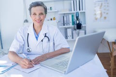 Docteur heureux regardant l'appareil-photo et écrivant sur le presse-papiers Images stock Docteur heureux regardant l'appareil-photo et écrivant sur le presse-papiers Images stock