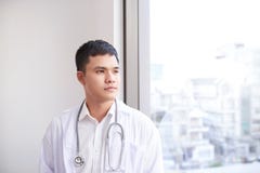 Doctor asiático de sexo masculino joven que mira fuera de la ventana el hospital imágenes de archivo libres de regalías Doctor asiático de sexo masculino joven que mira fuera de la ventana el hospital imágenes de archivo libres de regalías