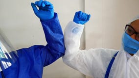 Doctor and nurse in personal protective equipment greet each other by touching elbows in the hospital during the covid-19 or