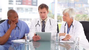 Doctor serio que habla con sus colegas sobre una PC de la tableta Doctor serio que habla con sus colegas sobre una PC de la tableta