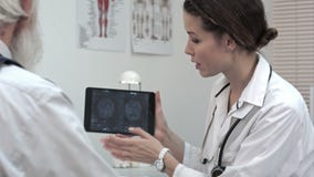 Doctor talking to patient about brain scans on tablet.