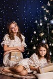 Dois amigos fêmeas com presentes aproximam a árvore de Natal foto de stock Dois amigos fêmeas com presentes aproximam a árvore de Natal foto de stock