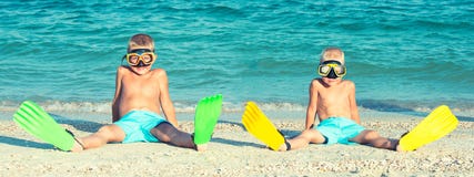 Dois irmãos nas máscaras e nas aletas estão sentando-se na praia Mergulhadores pequenos imagem de stock royalty free Dois irmãos nas máscaras e nas aletas estão sentando-se na praia Mergulhadores pequenos imagem de stock royalty free