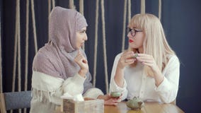 Dois muçulmanos e as mulheres caucasianos estão conversando o assento no café e no chá bebendo vídeos de arquivo Dois muçulmanos e as mulheres caucasianos estão conversando o assento no café e no chá bebendo vídeos de arquivo