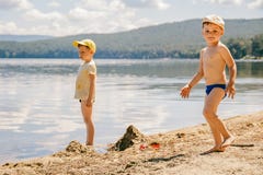 Dois rapazes pequenos nos tampões estão na costa arenosa do lago imagens de stock Dois rapazes pequenos nos tampões estão na costa arenosa do lago imagens de stock