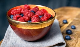 Dojrzałe słodkie malinki i czarne jagody w jaskrawym ceramicznym pucharze na szarym tabble płótnie na drewnianej kuchni wsiadają obrazy stock Dojrzałe słodkie malinki i czarne jagody w jaskrawym ceramicznym pucharze na szarym tabble płótnie na drewnianej kuchni wsiadają obrazy stock