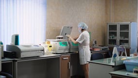 Doktorn på kliniken i ett vitt lag, som är i laboratoriumrummet, förlägger blodprov i en centrifugapparatur för lager videofilmer Doktorn på kliniken i ett vitt lag, som är i laboratoriumrummet, förlägger blodprov i en centrifugapparatur för lager videofilmer